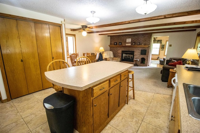 kitchen with light countertops, a fireplace, a ceiling fan, brown cabinetry, and a kitchen bar