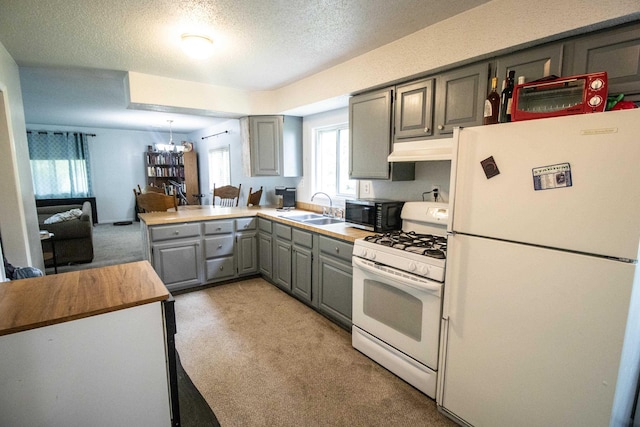 kitchen with white appliances, gray cabinetry, a sink, light carpet, and a chandelier