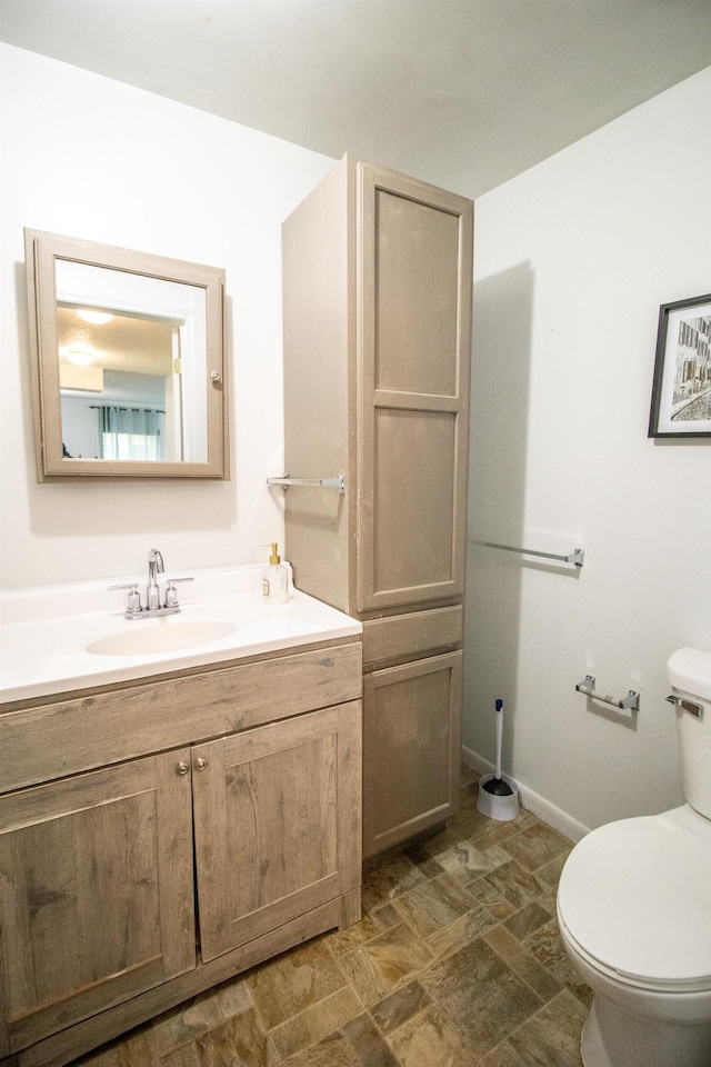 bathroom featuring toilet, stone finish floors, vanity, and baseboards