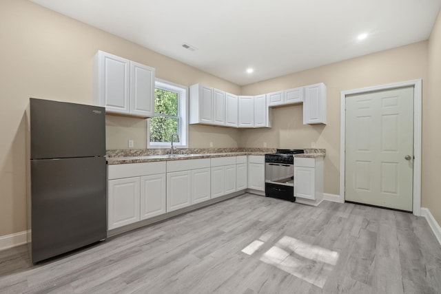 4624 Parman Rd, Stockbridge, MI 49285 - kitchen with freestanding refrigerator, black range with gas cooktop, a sink, light wood-style flooring, and white cabinetry