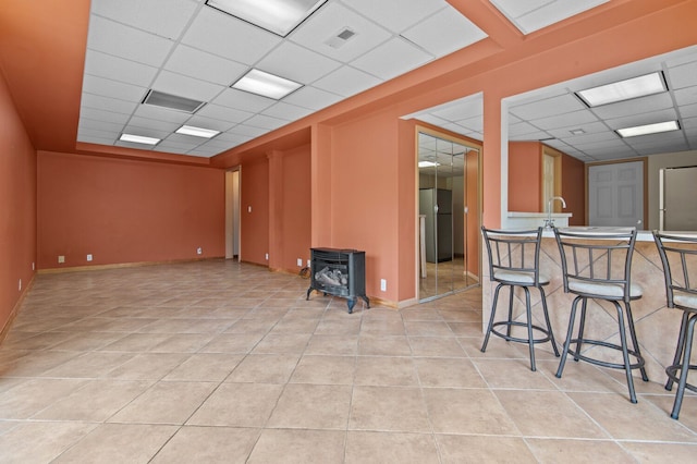 4900 Grass Lake Rd, White Lake, MI 48383 - unfurnished room featuring a paneled ceiling, a wood stove, light tile patterned flooring, a sink, and baseboards