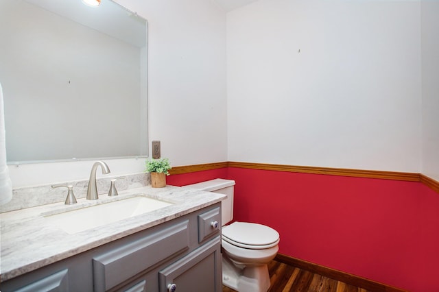 half bath featuring wood finished floors, vanity, and toilet