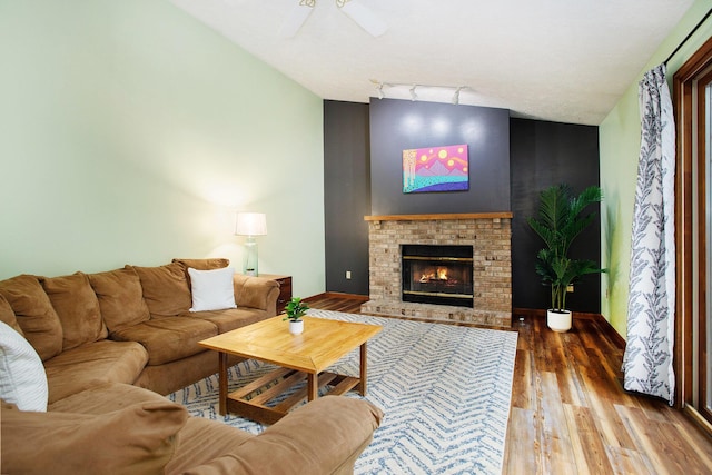 living room featuring wood finished floors, track lighting, vaulted ceiling, a fireplace, and ceiling fan