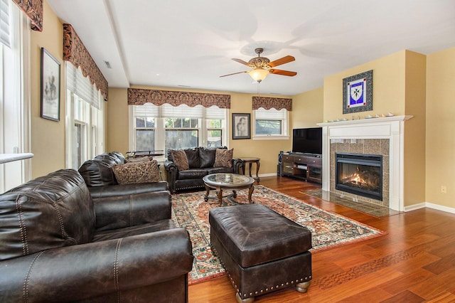 living area featuring ceiling fan, wood finished floors, a tile fireplace, and baseboards