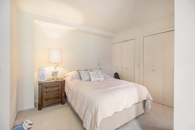 bedroom featuring multiple closets, light carpet, and baseboards