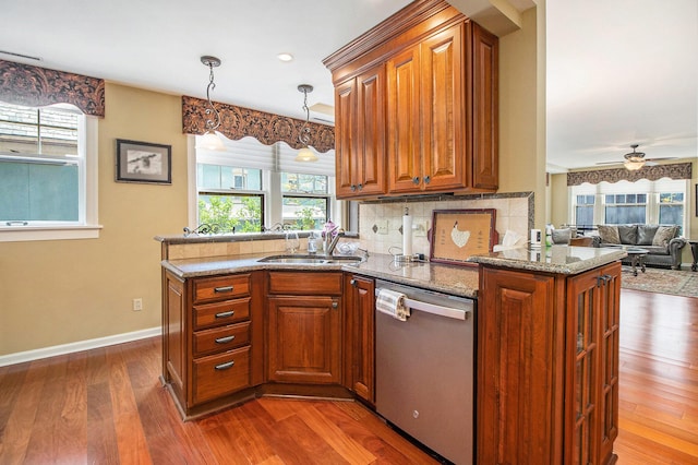 kitchen featuring dishwasher, a peninsula, brown cabinets, a sink, and wood finished floors