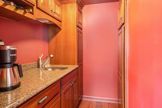 kitchen with a sink, light wood-style floors, light stone countertops, and baseboards