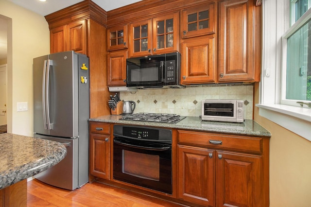 kitchen featuring black appliances, brown cabinets, decorative backsplash, light wood-type flooring, and glass insert cabinets