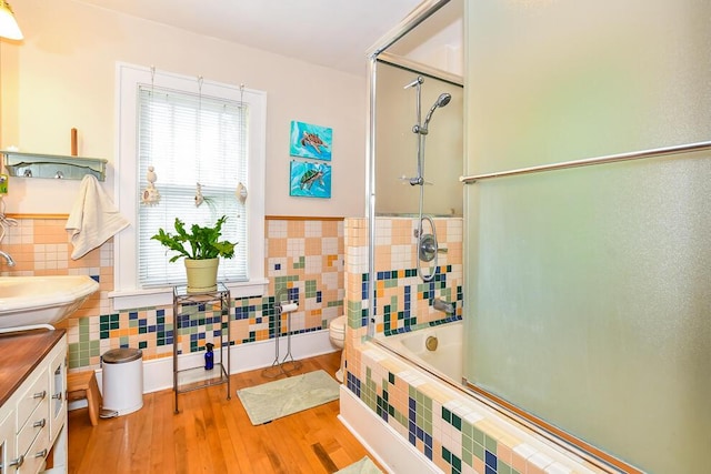full bathroom with tile walls, enclosed tub / shower combo, wood finished floors, toilet, and a wainscoted wall