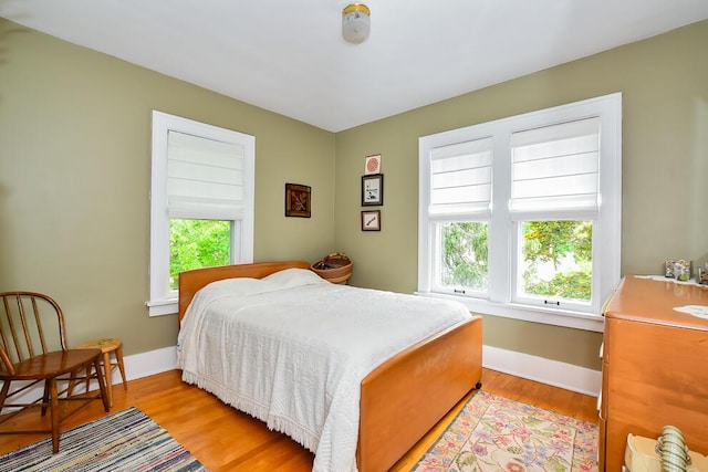 bedroom with multiple windows, light wood-style floors, and baseboards