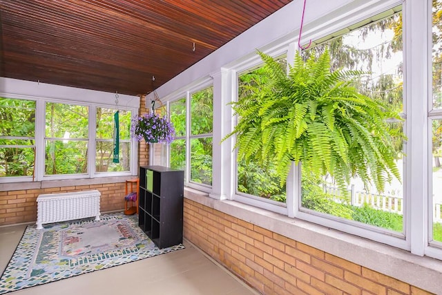 sunroom / solarium featuring radiator, brick wall, and finished concrete floors