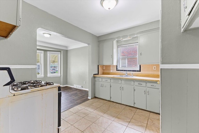 6905 Archdale St, Detroit, MI 48228 - kitchen featuring a sink, light countertops, white range with gas cooktop, white cabinetry, and a wainscoted wall