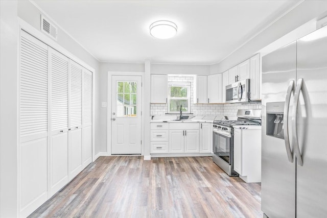 15016 Sunbury St, Livonia, MI 48154 - kitchen with appliances with stainless steel finishes, decorative backsplash, light countertops, white cabinets, and light wood finished floors