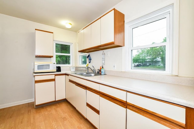 kitchen with white microwave, a sink, light countertops, and white cabinets