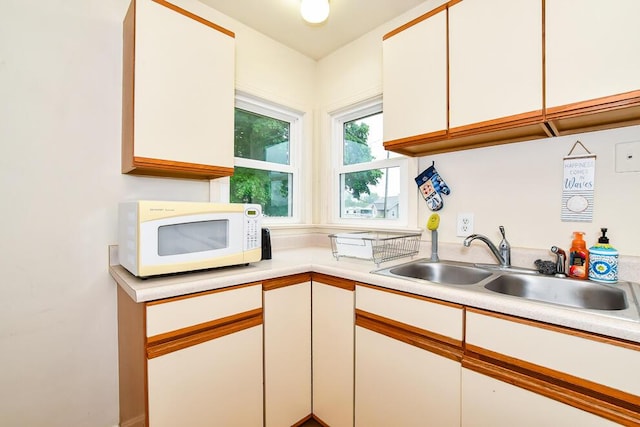 kitchen featuring white microwave, light countertops, white cabinets, and a sink