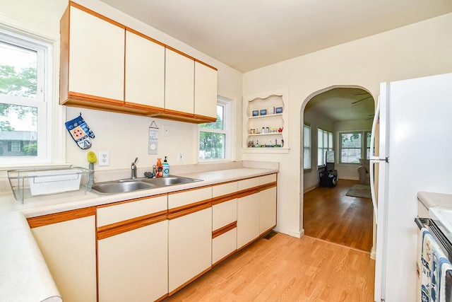 kitchen featuring arched walkways, light wood finished floors, a sink, and light countertops