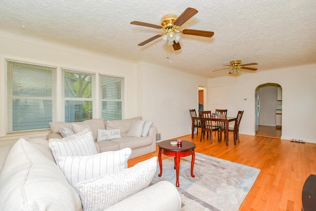 living room with arched walkways, a ceiling fan, a textured ceiling, and wood finished floors