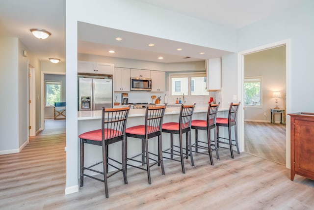 130 N Shore Dr Unit 8, South Haven, MI 49090 - kitchen with appliances with stainless steel finishes, light wood-type flooring, white cabinets, a peninsula, and baseboards
