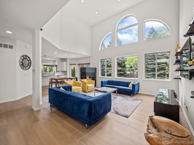 1231 Burns Dr, Troy, MI 48083 - living room with light wood-style floors, a towering ceiling, recessed lighting, baseboards, and a warm lit fireplace