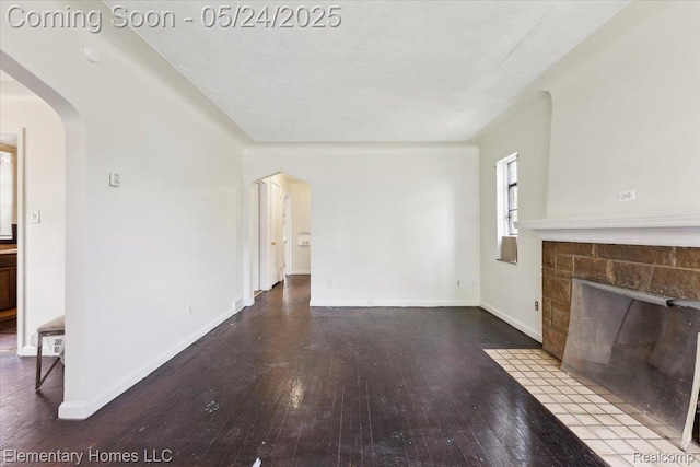 18965 Rutherford St, Detroit, MI 48235 - unfurnished living room featuring arched walkways, hardwood / wood-style flooring, a stone fireplace, and baseboards