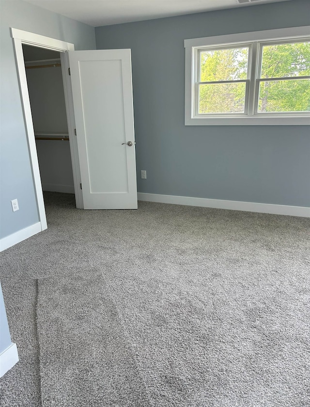 unfurnished bedroom with carpet, baseboards, a spacious closet, and a closet