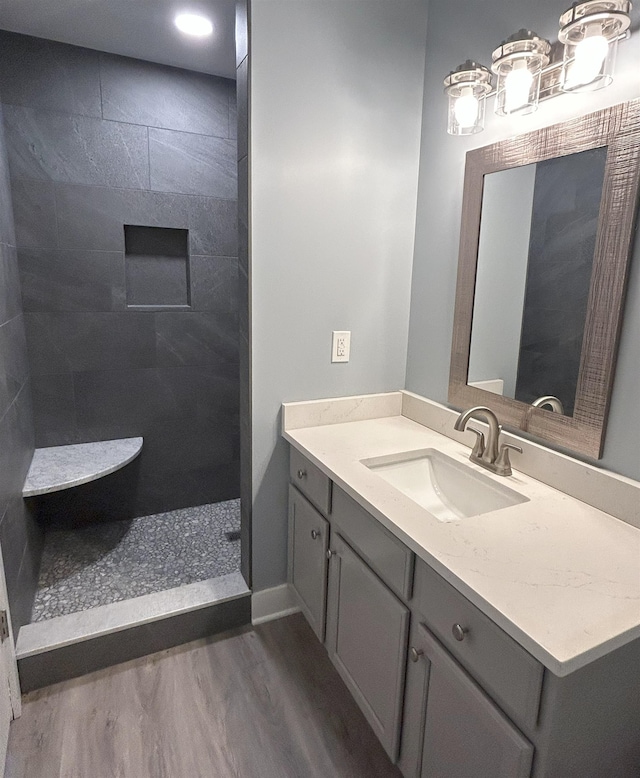 bathroom with wood finished floors, a tile shower, and vanity