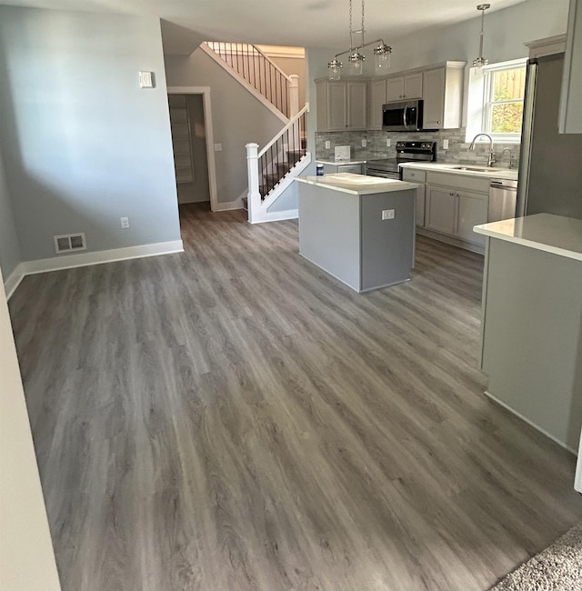 kitchen featuring stainless steel appliances, a kitchen island, a sink, decorative backsplash, and light countertops