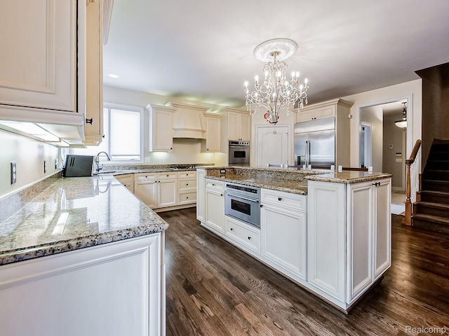 4575 Forest Edge Ln, West Bloomfield, MI 48323 - kitchen with stainless steel appliances, a kitchen island with sink, light stone countertops, a chandelier, and dark wood-style floors