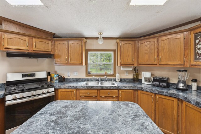 9168 Clewley Rd, Lachine, MI 49753 - kitchen with stainless steel gas range, a sink, under cabinet range hood, a textured ceiling, and brown cabinets
