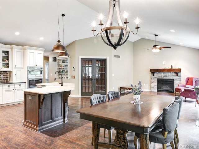 5076 Birch Ave, Lexington, MI 48450 - dining area featuring a fireplace, a chandelier, lofted ceiling, ceiling fan, and dark wood-style floors