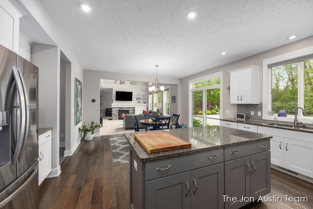 9012 N Wolven Ridge Ct, Rockford, MI 49341 - kitchen featuring stainless steel fridge with ice dispenser, a sink, a stone fireplace, a textured ceiling, and dark stone countertops