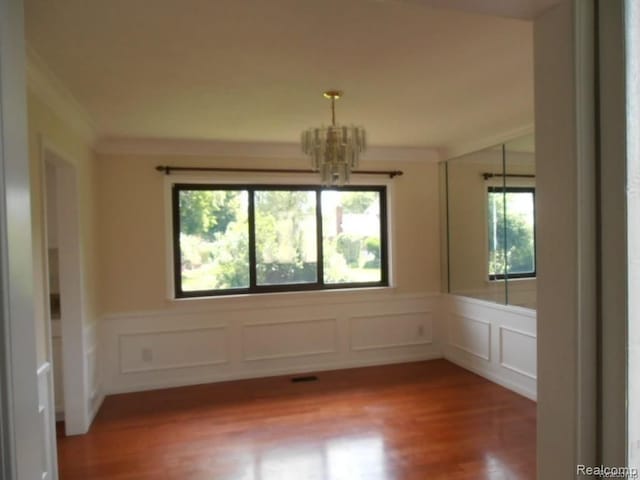 5086 Falmouth Dr, Troy, MI 48085 - spare room featuring a chandelier, crown molding, wood finished floors, a decorative wall, and wainscoting