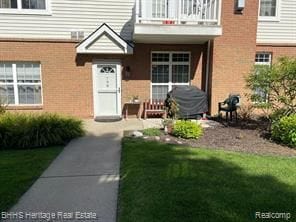 798 Olde English Cir, Howell, MI 48855 - view of exterior entry with a balcony, a yard, and brick siding