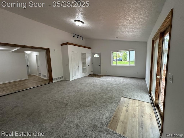 5399 Brobeck St, Flint, MI 48532 - unfurnished living room with vaulted ceiling, a textured ceiling, carpet, baseboards, and wood finished floors
