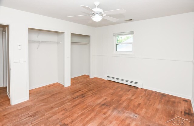 1466 Wilson Ave, Saginaw, MI 48638 - unfurnished bedroom featuring baseboard heating, multiple closets, light wood finished floors, and baseboards