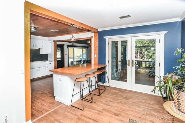 1466 Wilson Ave, Saginaw, MI 48638 - kitchen with white cabinets, light wood finished floors, ornamental molding, a kitchen breakfast bar, and french doors