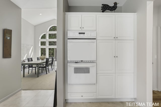 12993 144th Ave, Grand Haven, MI 49417 - kitchen with white double oven, lofted ceiling, white cabinetry, baseboards, and light tile patterned floors