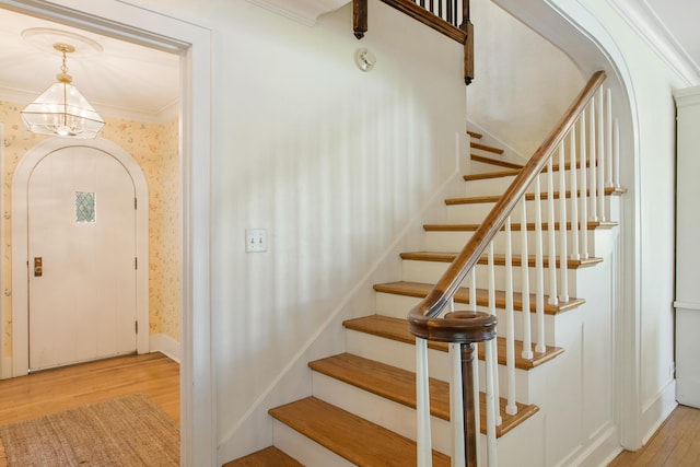 18957 N Fruitport Rd, Spring Lake, MI 49456 - stairway featuring wood finished floors, wallpapered walls, crown molding, a chandelier, and arched walkways