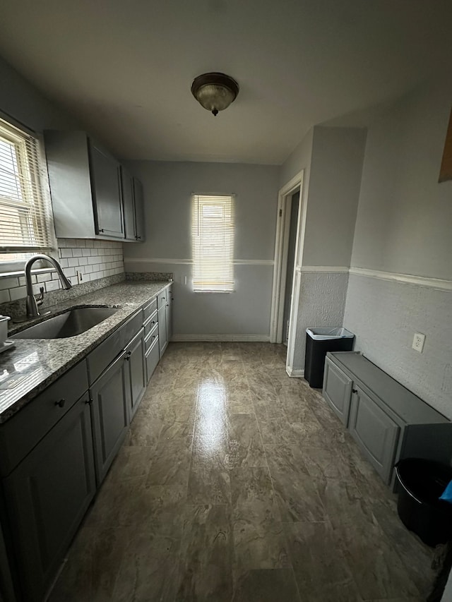 8603 Whitcomb St, Detroit, MI 48228 - kitchen featuring a sink, light stone countertops, decorative backsplash, baseboards, and a wainscoted wall