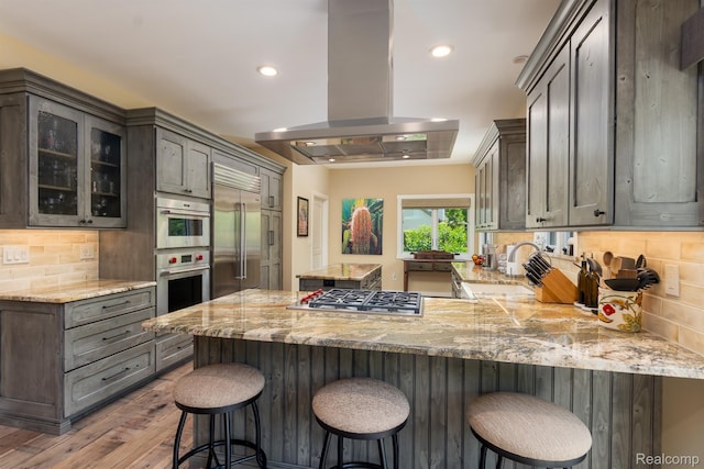 5502 E Alyssa Ct, White Lake, MI 48383 - kitchen with island exhaust hood, stainless steel appliances, a sink, hardwood / wood-style floors, and a peninsula