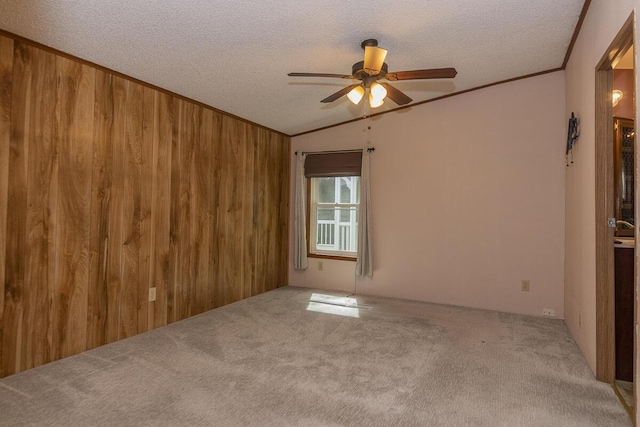 10303 Walnut Dr, Three Rivers, MI 49093 - carpeted empty room with a ceiling fan, a textured ceiling, vaulted ceiling, wooden walls, and ornamental molding