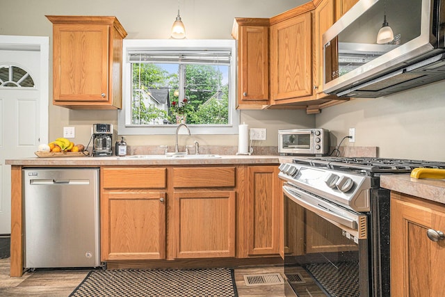 201 Page St NE, Grand Rapids, MI 49505 - kitchen featuring appliances with stainless steel finishes, a sink, light countertops, light wood-style flooring, and hanging light fixtures