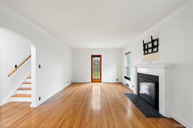 99 Wenonah Dr, Pontiac, MI 48341 - unfurnished living room featuring light wood finished floors, a fireplace with flush hearth, stairway, arched walkways, and baseboards