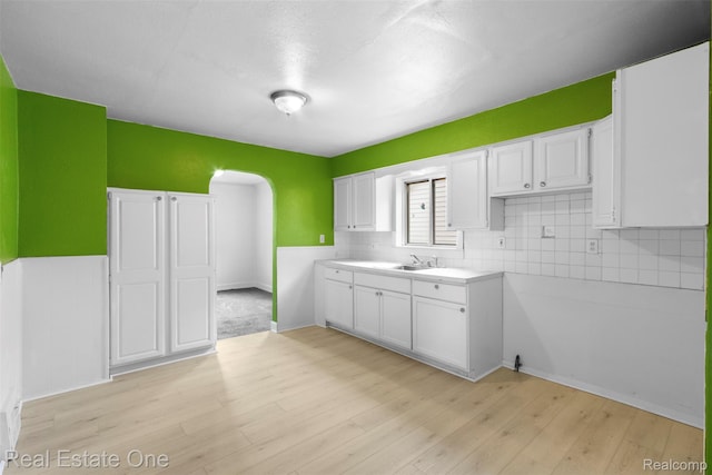 8492 Meadow Ave, Warren, MI 48089 - kitchen featuring arched walkways, white cabinetry, light wood-type flooring, backsplash, and light countertops