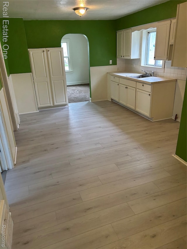 8492 Meadow Ave, Warren, MI 48089 - kitchen with arched walkways, a sink, backsplash, light wood finished floors, and white cabinets