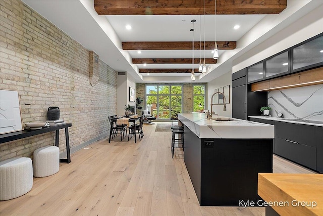 52 E 8th St Ste 210, Holland, MI 49423 - kitchen featuring modern cabinets, brick wall, beam ceiling, dark cabinetry, and an island with sink
