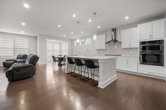 2610 Ironton Dr, Commerce Twp, MI 48382 - kitchen featuring wall chimney exhaust hood, double wall oven, a kitchen island with sink, gas cooktop, and a sink