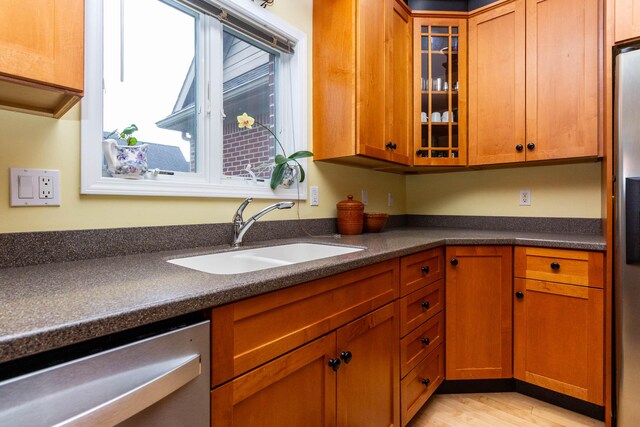 7009 Suncrest Dr, Saline, MI 48176 - kitchen with stainless steel dishwasher, a sink, dark countertops, light wood finished floors, and glass insert cabinets