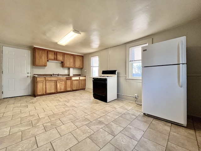 1837 Franklin St, Muskegon, MI 49441 - kitchen with freestanding refrigerator, gas stove, a sink, brown cabinets, and wainscoting
