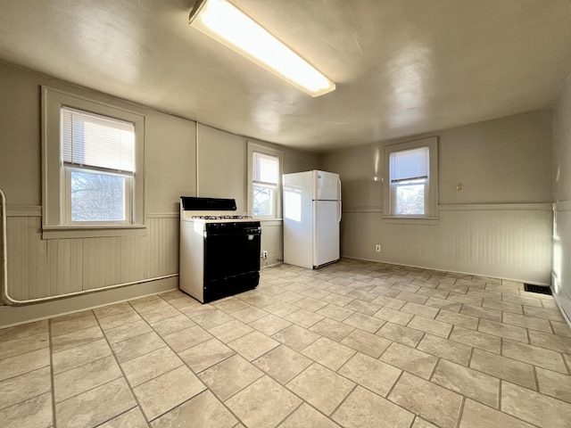 1837 Franklin St, Muskegon, MI 49441 - kitchen with freestanding refrigerator, gas range oven, a wainscoted wall, and plenty of natural light